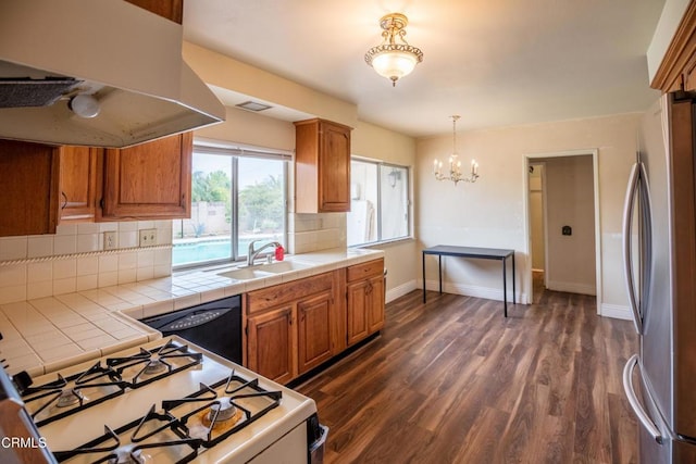 kitchen with freestanding refrigerator, a sink, under cabinet range hood, gas range gas stove, and tile counters