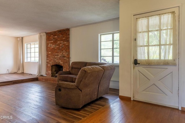 living room featuring hardwood / wood-style floors, a fireplace, a textured ceiling, a baseboard heating unit, and baseboards