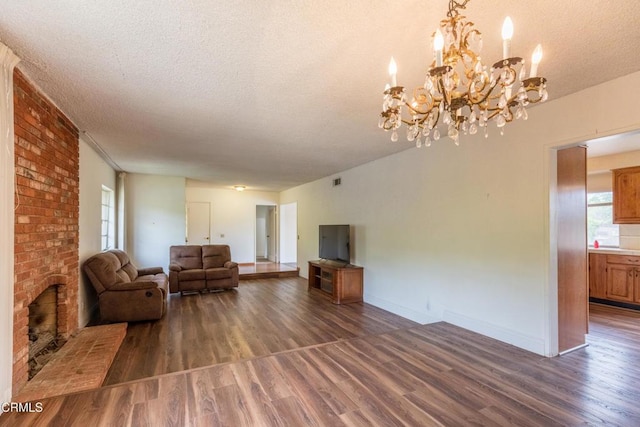 living area with a chandelier, wood finished floors, a textured ceiling, baseboards, and a brick fireplace