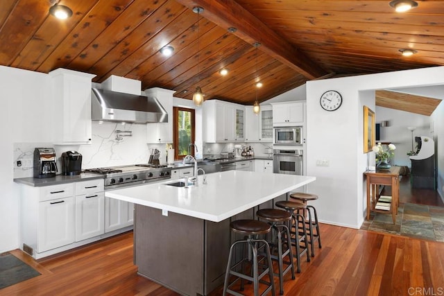 kitchen featuring stainless steel appliances, wall chimney range hood, dark wood finished floors, a center island with sink, and glass insert cabinets
