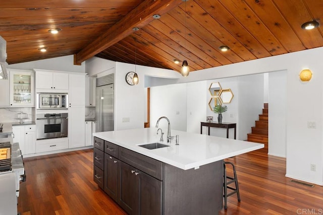 kitchen with built in appliances, a sink, dark wood finished floors, white cabinetry, and a kitchen bar