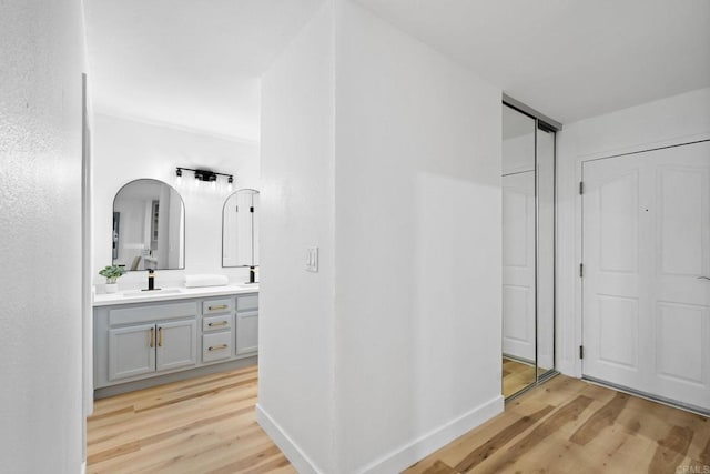 hallway with light wood finished floors, a sink, and baseboards