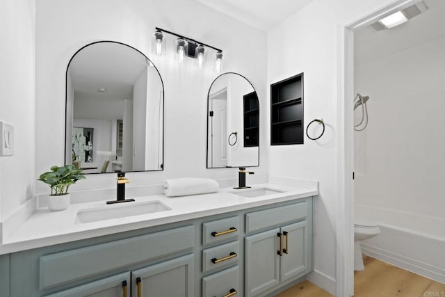 bathroom with double vanity, toilet, wood finished floors, and  shower combination