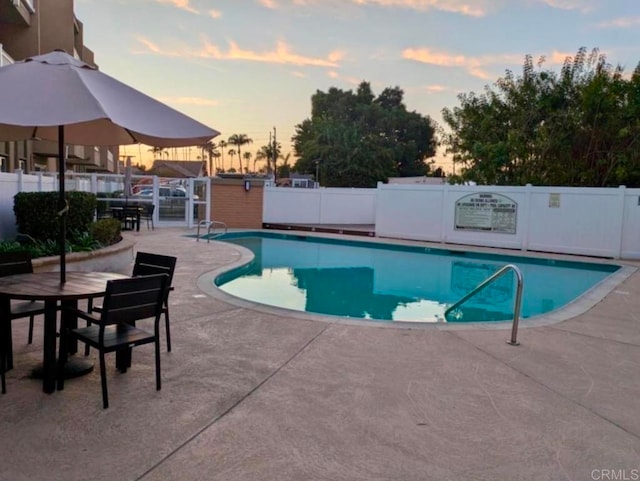 community pool with a patio, fence, and outdoor dining space