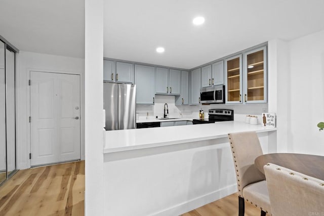 kitchen featuring appliances with stainless steel finishes, a sink, glass insert cabinets, light wood-type flooring, and light countertops