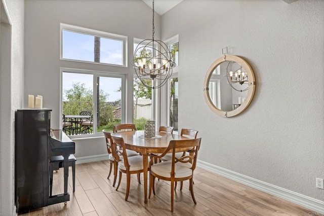 dining area with a chandelier, baseboards, light wood-style flooring, and high vaulted ceiling