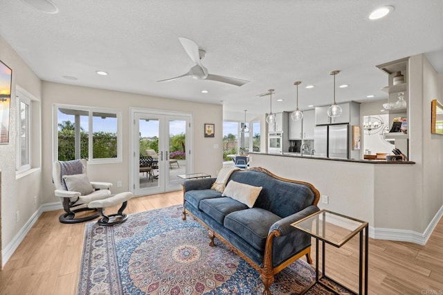 living area featuring french doors, ceiling fan, baseboards, light wood-type flooring, and a textured ceiling