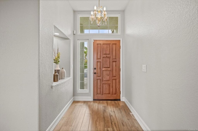 foyer entrance featuring baseboards, light wood-style floors, and a chandelier