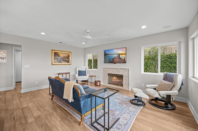 living room with a glass covered fireplace, light wood-style floors, baseboards, recessed lighting, and a ceiling fan