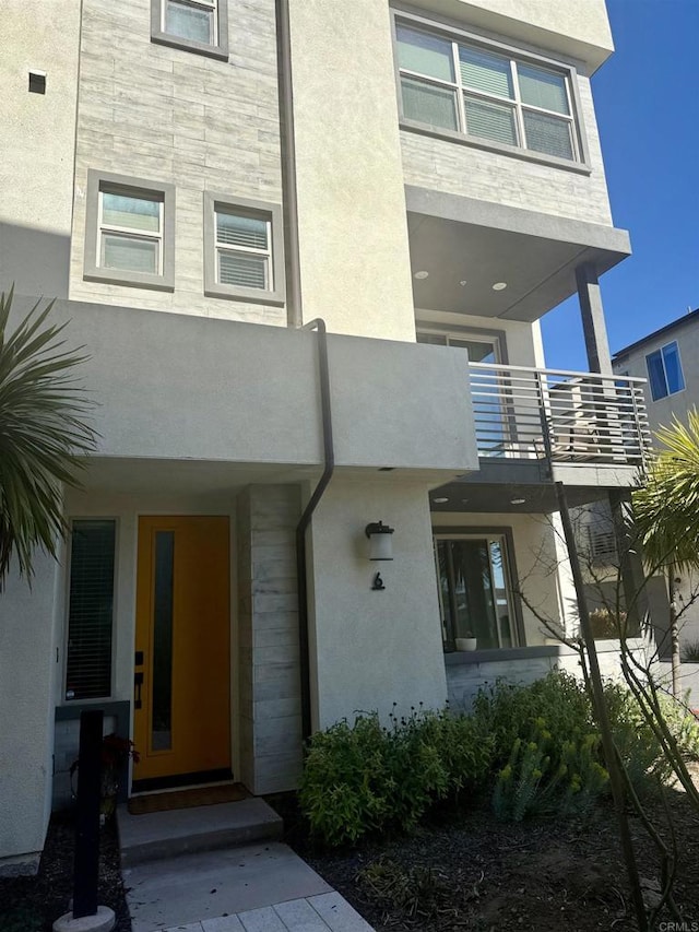 view of exterior entry with a balcony, stucco siding, and stone siding