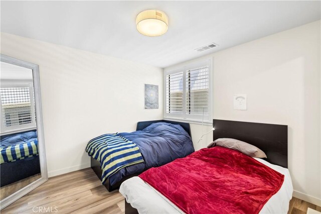 bedroom with multiple windows, wood finished floors, and baseboards
