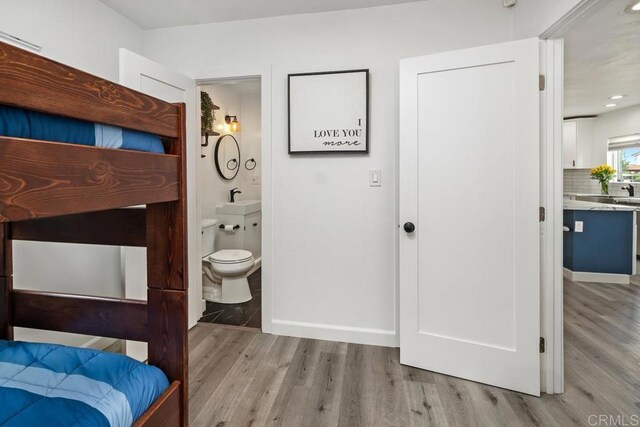 bedroom featuring wood finished floors, ensuite bathroom, baseboards, and recessed lighting