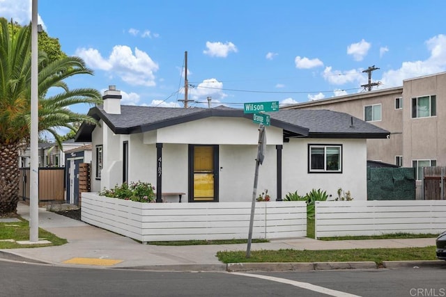 bungalow featuring stucco siding, roof with shingles, and a chimney