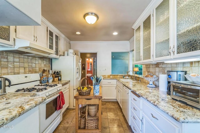 kitchen with white appliances, under cabinet range hood, a sink, backsplash, and crown molding