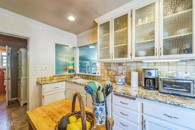 kitchen featuring decorative backsplash, ornamental molding, glass insert cabinets, white cabinetry, and dark tile patterned floors