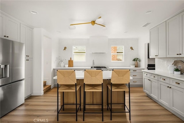 2153 Stanbridge Ave, Long Beach, CA 90815 - kitchen with stainless steel fridge with ice dispenser, tasteful backsplash, a kitchen bar, light wood finished floors, and light countertops