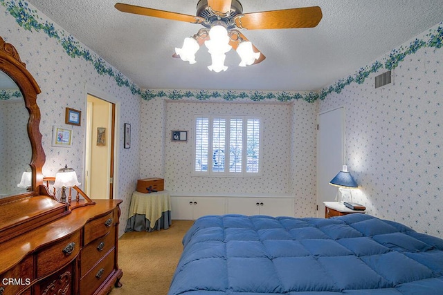 bedroom featuring light colored carpet, a textured ceiling, wallpapered walls, and a ceiling fan
