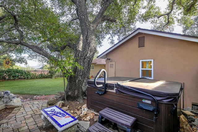 view of green lawn with a hot tub and a patio area