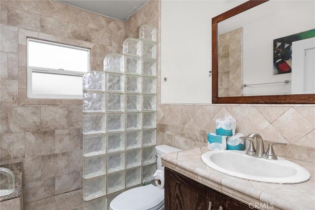 full bath with tile walls, walk in shower, toilet, and vanity