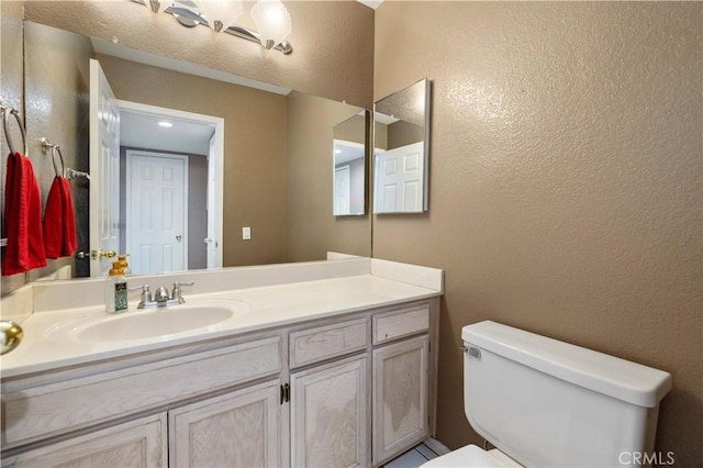 bathroom with a textured wall, toilet, and vanity