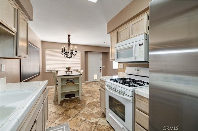 kitchen with white appliances, tile counters, a chandelier, pendant lighting, and a sink