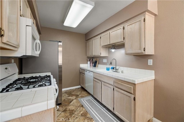 kitchen with a sink, white appliances, tile counters, baseboards, and light brown cabinetry