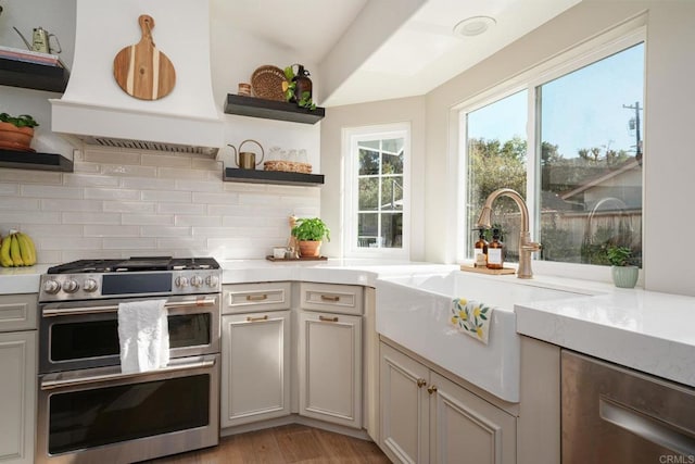 kitchen featuring open shelves, stainless steel appliances, custom range hood, a sink, and tasteful backsplash