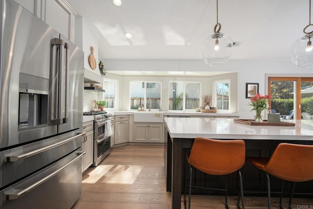 kitchen featuring high quality appliances, light countertops, a breakfast bar area, light wood-type flooring, and a sink