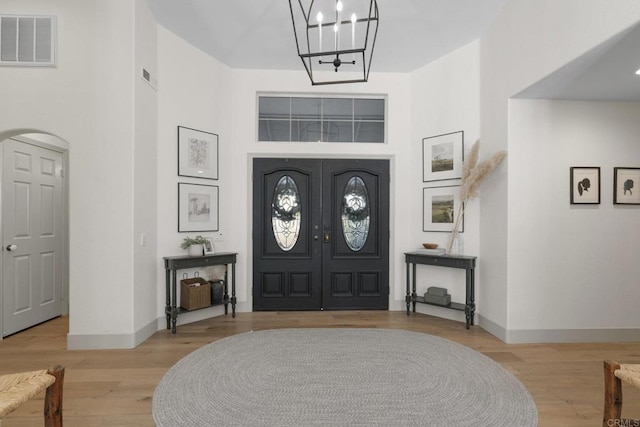 foyer entrance with baseboards, arched walkways, wood finished floors, a chandelier, and a towering ceiling