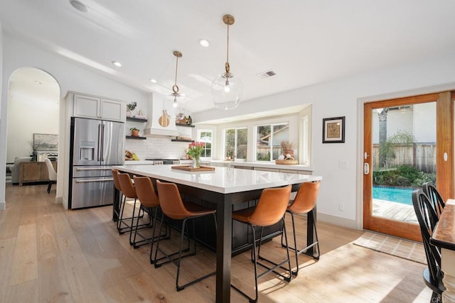 kitchen with stainless steel refrigerator with ice dispenser, open shelves, light countertops, light wood-style floors, and recessed lighting