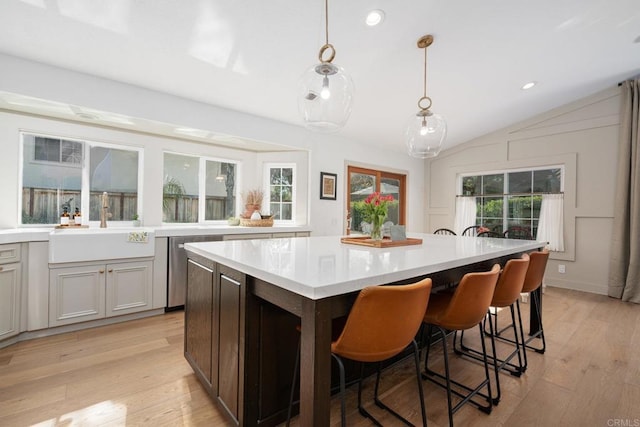 kitchen with stainless steel dishwasher, light countertops, light wood-type flooring, a kitchen island, and lofted ceiling