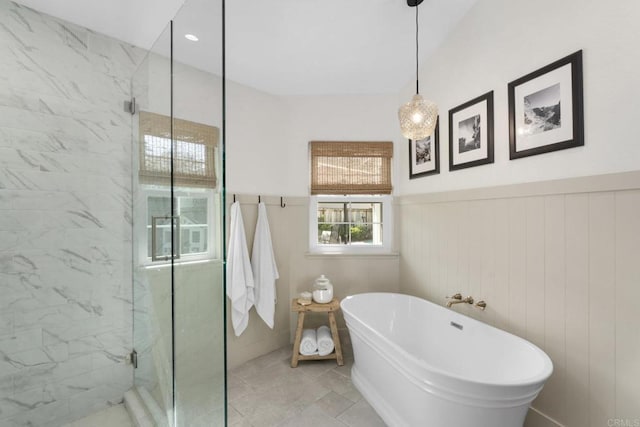 bathroom featuring a marble finish shower, a soaking tub, and a wainscoted wall