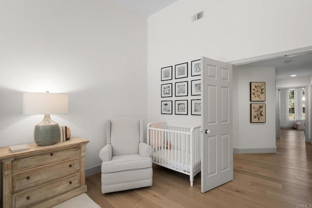 bedroom with light wood-style flooring, a crib, and baseboards