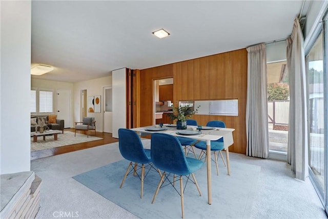 dining space featuring light colored carpet and wood walls