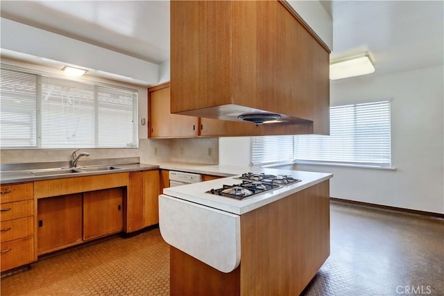 kitchen with a sink, a peninsula, stainless steel gas stovetop, light floors, and brown cabinets