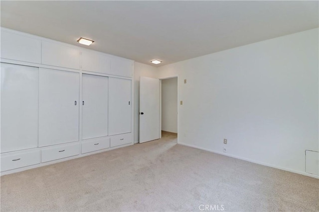 unfurnished bedroom featuring light colored carpet, a closet, and baseboards
