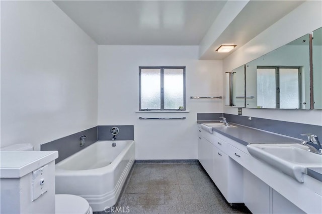 bathroom featuring baseboards, a garden tub, double vanity, and toilet