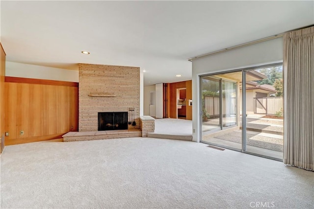 unfurnished living room with carpet, a stone fireplace, wood walls, and recessed lighting