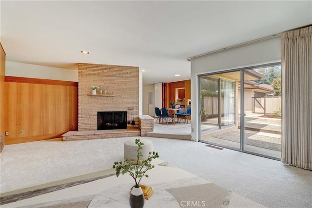 living room featuring a stone fireplace, carpet, and wooden walls