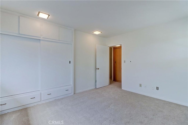 unfurnished bedroom featuring light colored carpet, a closet, and baseboards