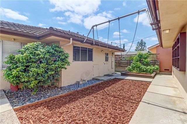 view of side of home with stucco siding, fence, and a garden