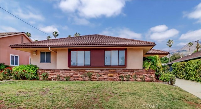 back of property featuring stone siding, stucco siding, a yard, and a tiled roof