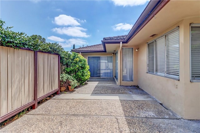 entrance to property featuring stucco siding, a tile roof, fence, and a patio