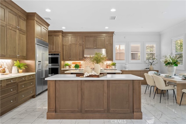 kitchen with appliances with stainless steel finishes, a kitchen island, light marble finish flooring, light countertops, and ornamental molding