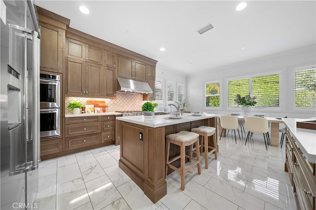 kitchen featuring under cabinet range hood, light marble finish floors, plenty of natural light, crown molding, and stainless steel double oven