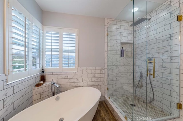 bathroom with tile walls, a freestanding tub, a shower stall, wood finished floors, and a wainscoted wall
