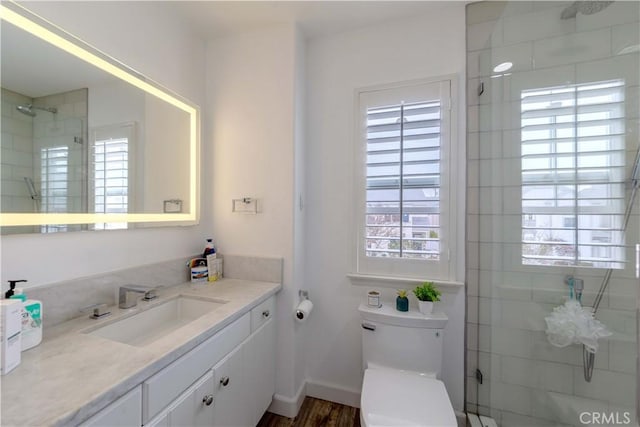 bathroom with a tile shower, toilet, vanity, and wood finished floors