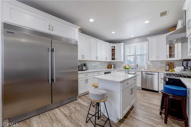 kitchen featuring stainless steel appliances, backsplash, a breakfast bar area, glass insert cabinets, and white cabinetry