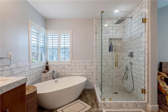 full bathroom with tile walls, a shower stall, a soaking tub, wainscoting, and vanity
