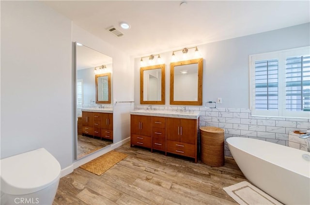 bathroom with tile walls, wood finished floors, a freestanding bath, double vanity, and wainscoting